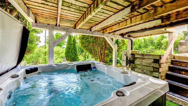 Un jacuzzi bajo una pérgola de madera con vista a zonas verdes.