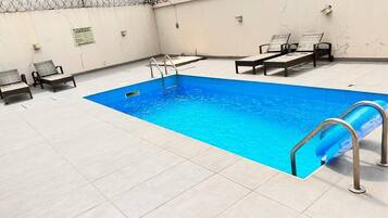 Ein rechteckiger Pool mit Fliesenveranda, Metallleiter und zwei Liegestühlen.