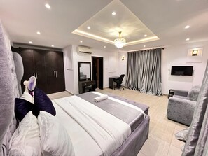 A modern hotel room with a large bed, a desk, a chair, a TV, and a wardrobe. - Service Apartment Hub (Lagos)