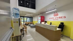 A reception desk with a water dispenser, seating area, and a sign reading "COZY CUBES HOSTEL". - Cozy Cubes (Ho Chi Minh City)