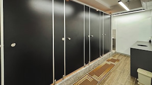 A row of black lockers with white trim, a tiled floor, and a modern bathroom with a sink and toilet. - Cozy Cubes (Ho Chi Minh City)