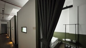 A hotel room with a bed, a small shelf with toiletries, a mirror, and a curtain. - Cozy Cubes (Ho Chi Minh City)