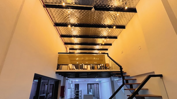 A modern interior with a staircase leading to a mezzanine level, wooden benches, and a dining area. - Cozy Cubes (Ho Chi Minh City)