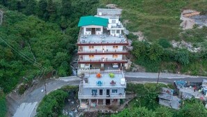 Un edificio de varios pisos con techo verde, rodeado de exuberante vegetación y un camino sinuoso.