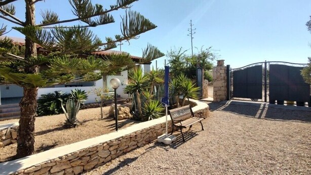 A landscaped garden with a stone wall, a bench, and various plants. - Residence Lo Zodiaco (Lampedusa)