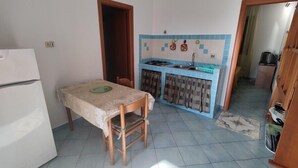 A compact kitchen with a dining table and chairs, a small sink, and a tiled backsplash. - Residence Lo Zodiaco (Lampedusa)