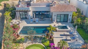 Une maison moderne dotée d’une grande piscine, d’un espace salon extérieur et d’un aménagement paysager luxuriant.