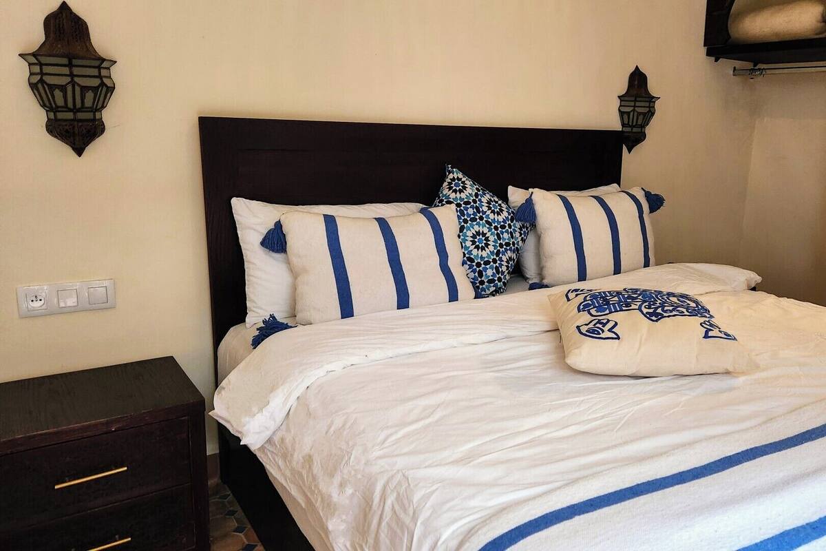 Una cama bien hecha con ropa de cama a rayas blancas y azules, un cabecero de madera oscura y apliques decorativos en la pared.