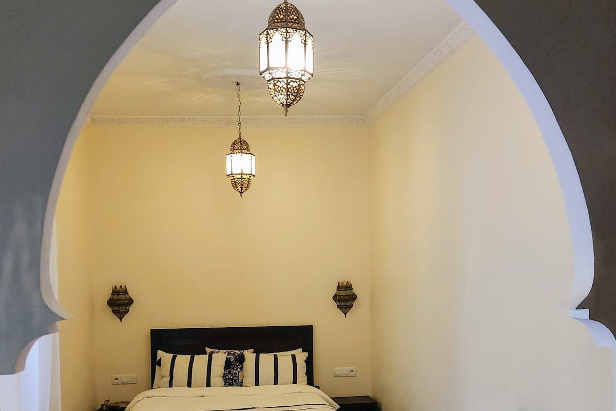 Un dormitorio con una cama, una mesa redonda de madera, un sofá y dos lámparas fijadas a la pared.