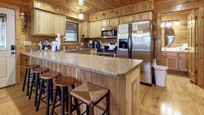 A kitchen with wooden cabinets, a stainless steel refrigerator, a granite countertop, and bar stools.