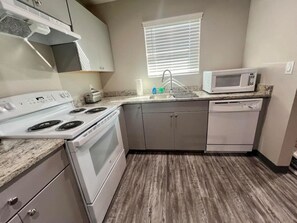 A kitchen with a stove, microwave, sink, and cabinets.