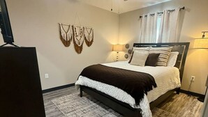 Une chambre avec un lit, un ventilateur de plafond, un téléviseur fixé au mur et un tapis.