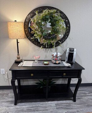 A black desk with a coffee maker, a glass of water, and a decorative wreath on the wall behind it. - Your Peaceful Retreat (Portales)