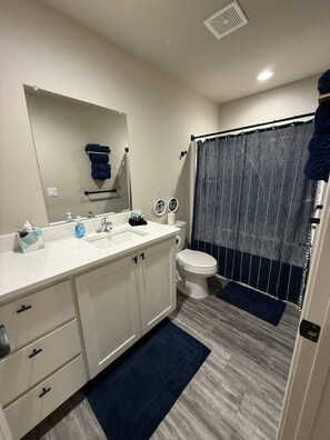 A bathroom with a white sink, mirror, and toilet, a blue shower curtain, and a dark blue rug. - Your Peaceful Retreat (Portales)