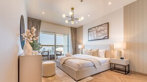 A modern bedroom with a large bed, bedside lamps, a side table, a vase with flowers, and a view of the city through large windows.