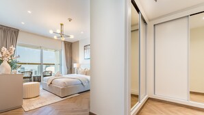 A modern bedroom with a large bed, bedside tables, a desk, and a view of the city through floor-to-ceiling windows.