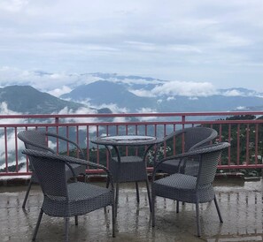 A balcony with wicker furniture and a view of mountains and clouds. - Hotel Basa Palace By GRB (Theog)