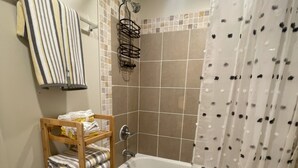 Et badeværelse med bruser, toilet og en hylde med sammenfoldede håndklæder.