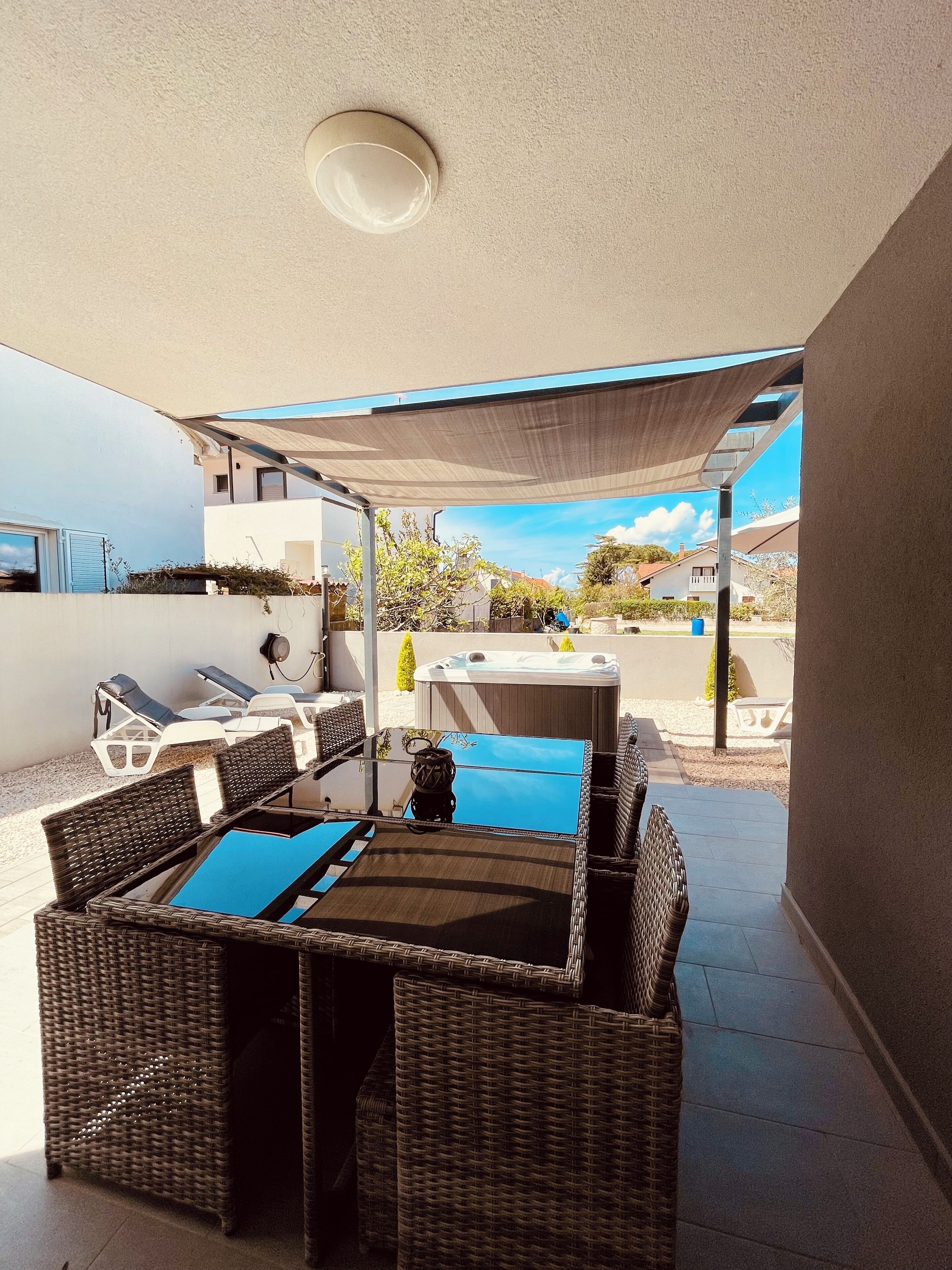 A covered patio area with wicker furniture, a hot tub, and a view of the neighborhood.