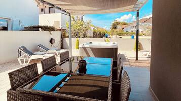 A covered patio area with wicker furniture, a hot tub, and a view of the neighborhood.
