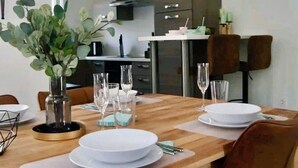 Un comedor moderno con una mesa de madera dispuesta para cuatro personas, una planta en maceta y una lámpara colgante negra.
