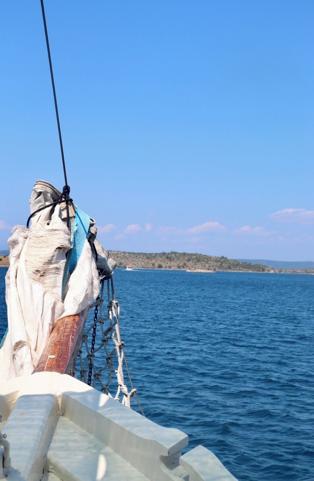 A boat's bow with ropes and a net, calm sea, and a distant shoreline.