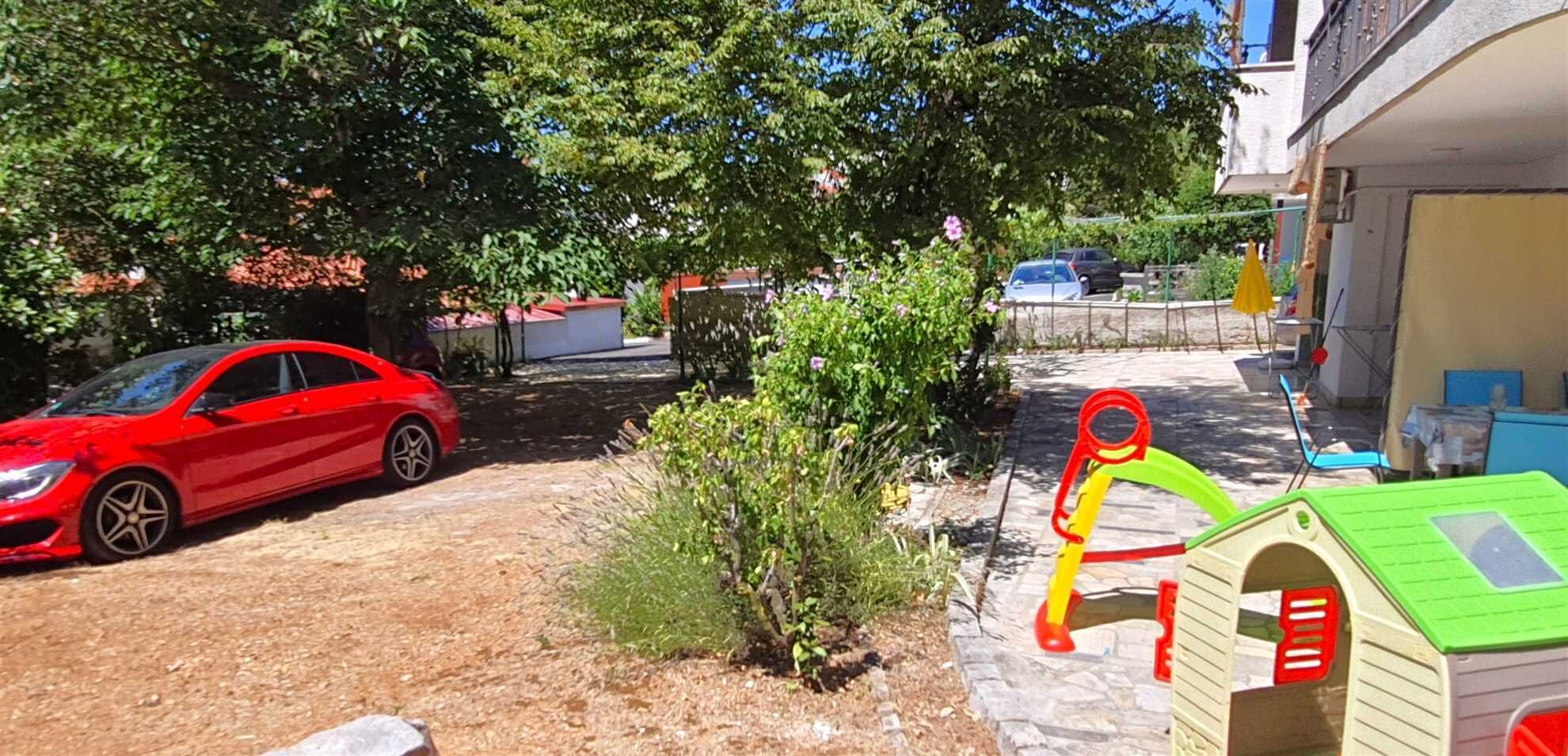 En röd bil parkerad på en uppfart med en liten trädgård och en lekställning.