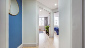 Un pasillo con pared azul, un espejo redondo y una cama con cubrecama azul al fondo.