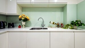 Una cocina moderna con un lavamanos, un hervidor, un tostador, un florero con flores, una botella de vino y una planta en maceta.