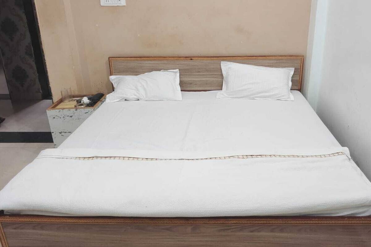 A bed with a wooden headboard, white bedding, and a small bedside table with a lamp.