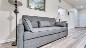 Ein graues Sofa mit Kissen, eine Stehlampe und ein gerahmtes Bild an der Wand.