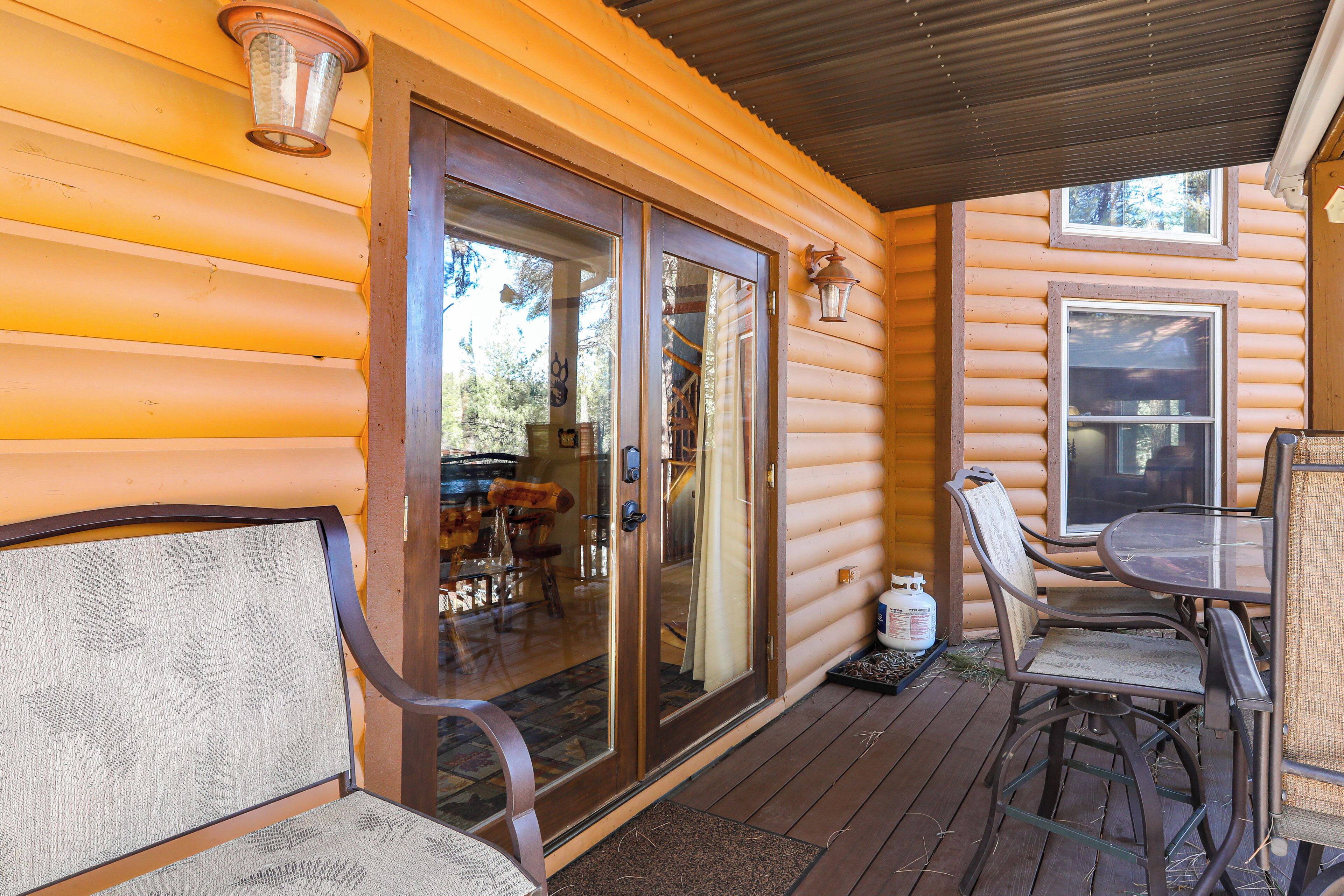 A log cabin with a covered deck, a sliding glass door, and a dining area with chairs and a table.