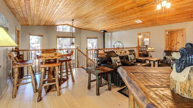 Un vaste espace de vie doté d’un plafond en bois, d’un ensemble de canapés, d’une table à manger avec des chaises et d’un escalier menant à un niveau supérieur.
