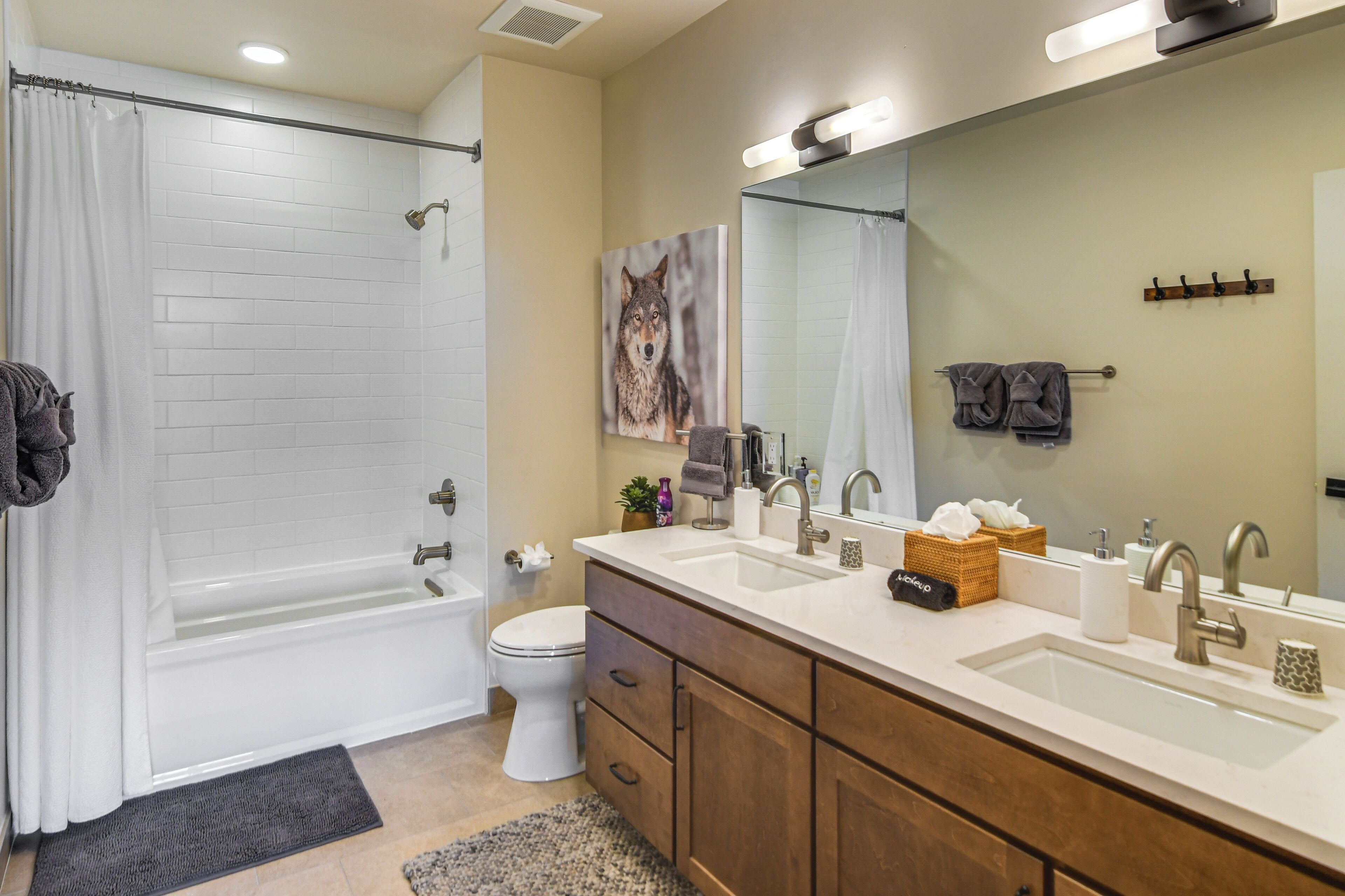 A modern bathroom with a bathtub, two sinks, a toilet, and a large mirror.