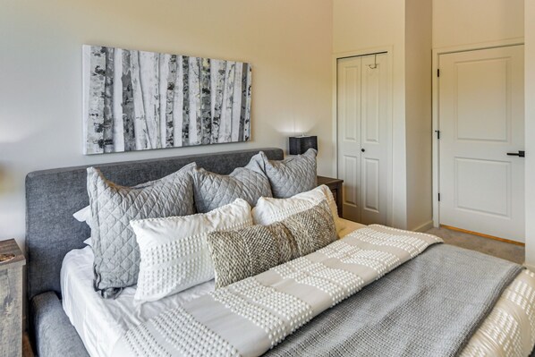 A bedroom with a bed, pillows, a wall-mounted artwork, a bedside table, and a door. - Near Hiking & Biking: Winter Park Mtn-view Haven! (Winter Park)
