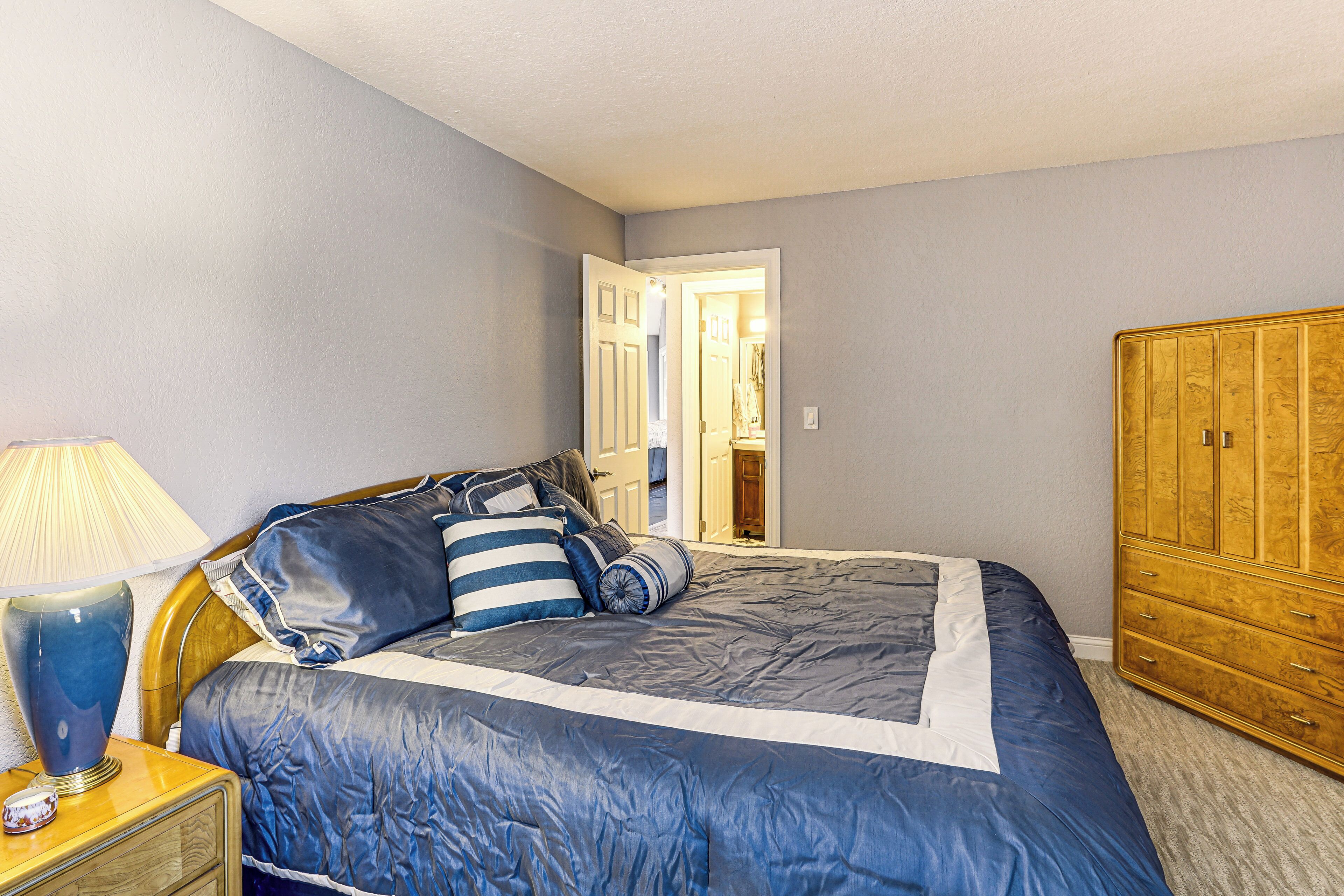 Un dormitorio con cama, mesita de noche, lámpara y armario de madera.