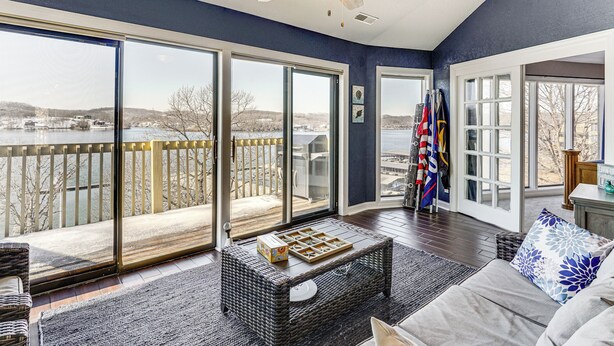 A spacious living room with a large sliding glass door leading to a balcony overlooking a body of water. - Boat, Swim & Enjoy Lake Views: Osage Beach Retreat (Osage Beach)