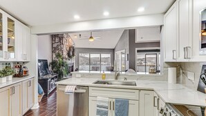 A modern kitchen with white cabinets, a stainless steel dishwasher, and a large island with a sink. - Boat, Swim & Enjoy Lake Views: Osage Beach Retreat (Osage Beach)