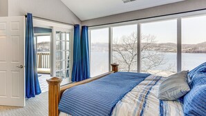 A bedroom with a large window, a bed with blue bedding, and a view of a lake. - Boat, Swim & Enjoy Lake Views: Osage Beach Retreat (Osage Beach)