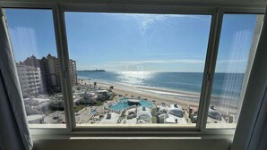 Vista desde una ventana con una playa, piscina y edificios circundantes.