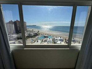 A view from a window overlooking a beach, a pool, and surrounding buildings.