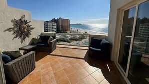 Un balcón con mobiliario exterior, un adorno de sol y vista a la playa y al océano.