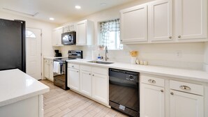 A modern kitchen with white cabinetry, stainless steel appliances, and a large window with curtains.