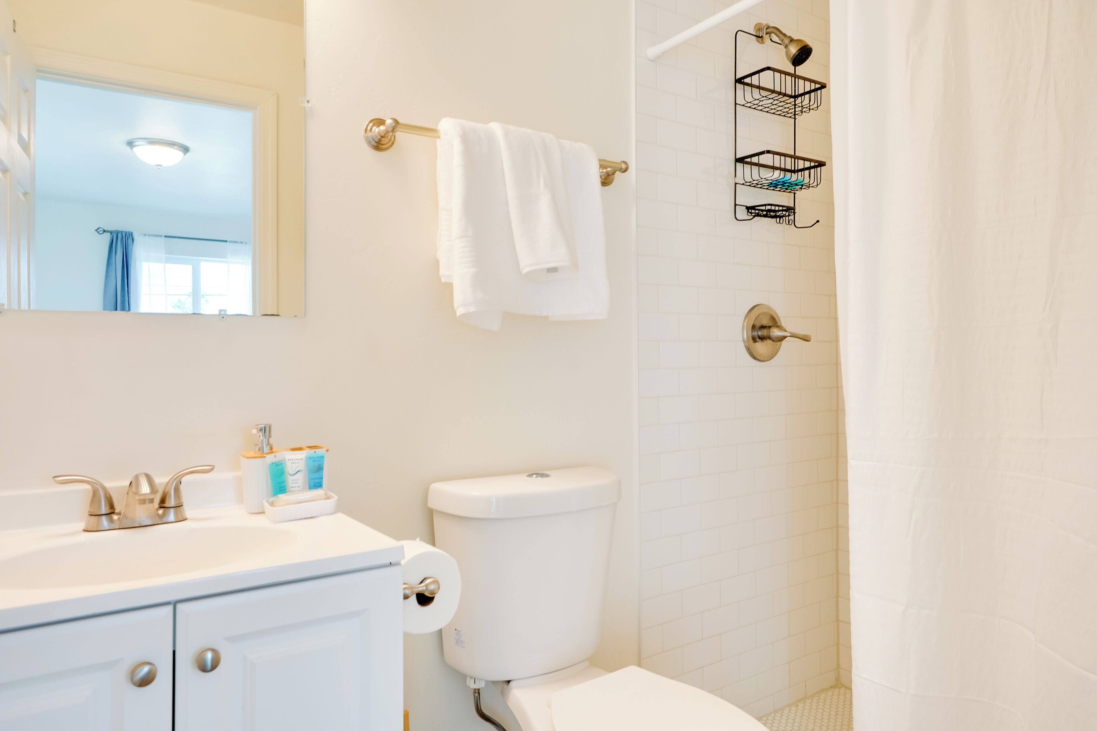 A bathroom with a white sink, toilet, and shower curtain. There is a towel rack with a white towel and a shower caddy.
