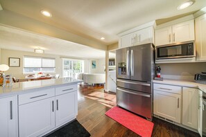 Une cuisine moderne avec des meubles blancs, des appareils en acier inoxydable et un tapis à motifs rouges.