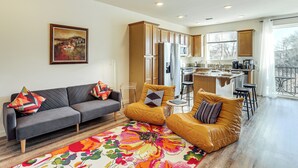 A modern living room with a sofa, armchairs, and a colorful rug. A kitchen with wooden cabinets and a dining area with stools is visible in the background. - 4 Mi to Dtwn: Family-friendly Townhome in Reno (Reno)