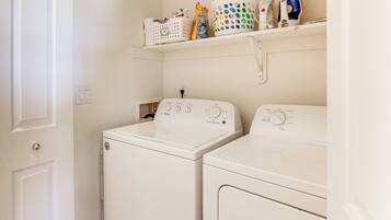 A laundry room with two white front-loading washing machines and a shelf above containing laundry supplies.
