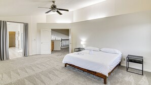 Een slaapkamer met een bed, een nachtkastje, een plafondventilator en een deur naar een andere kamer.
