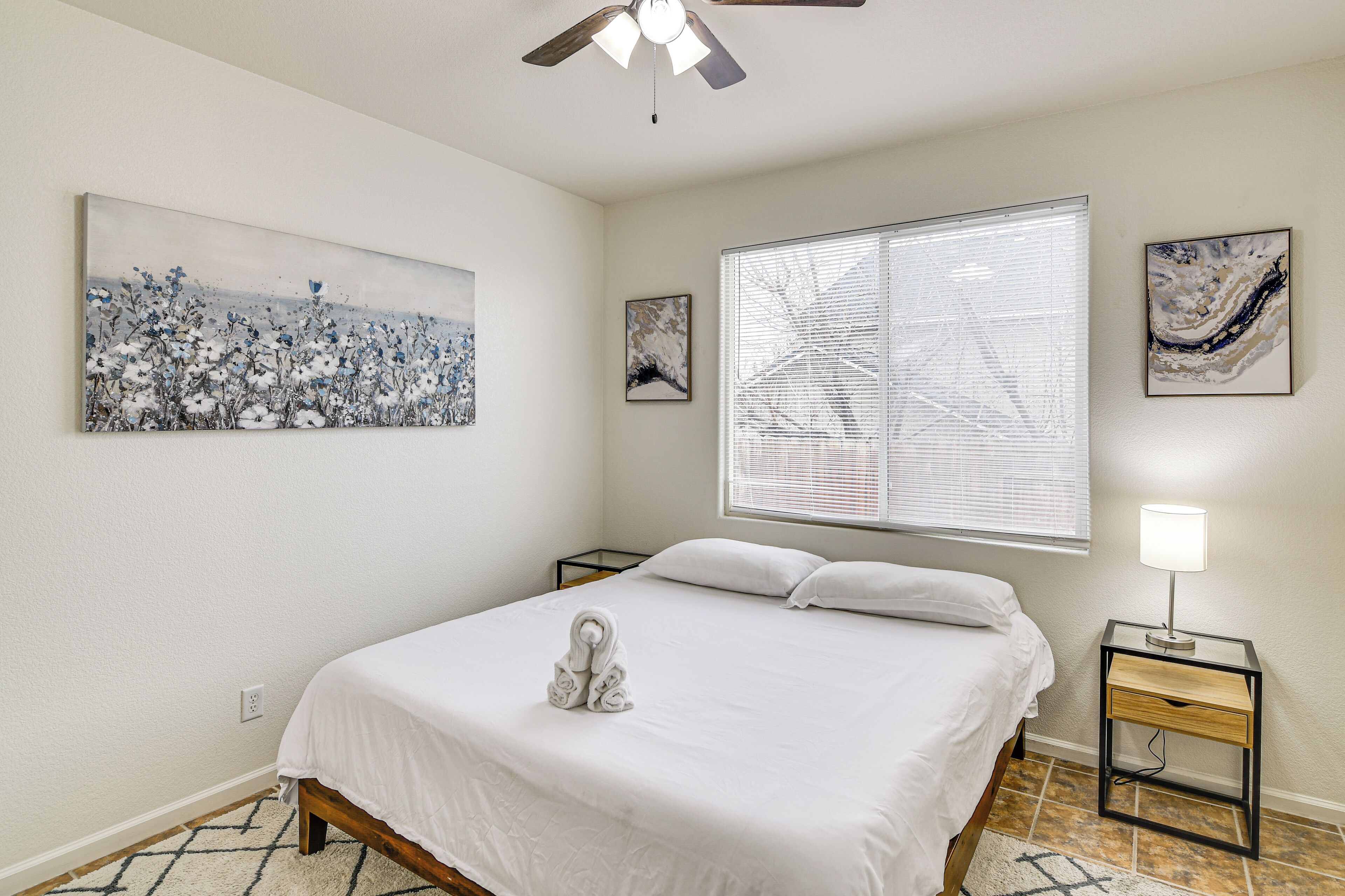 A neatly made bed with a towel, a ceiling fan, and artwork on the walls.