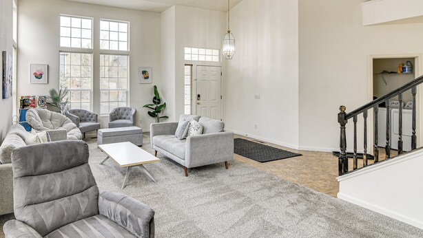 Een ruime woonkamer met een grijze zithoek, een salontafel en een trap naar een hoger gelegen verdieping.
